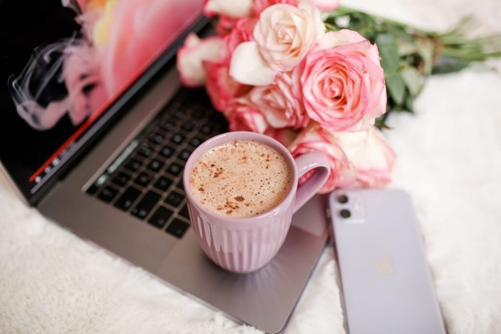 Feminine workspace aesthetic image including a phone laptop flowers and coffee