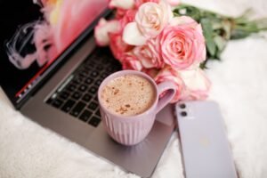 Feminine workspace aesthetic image including a phone laptop flowers and coffee