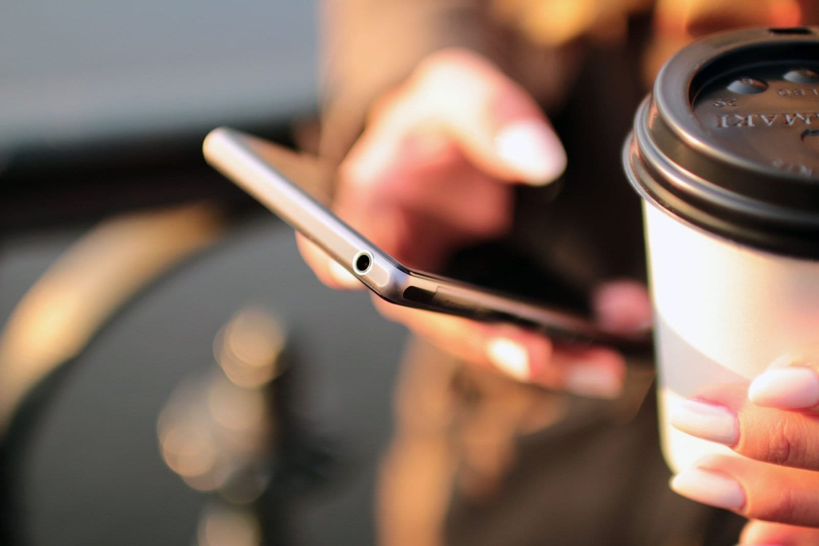 closeup photo of lady's hand holding a smartphone and a takeaway coffee